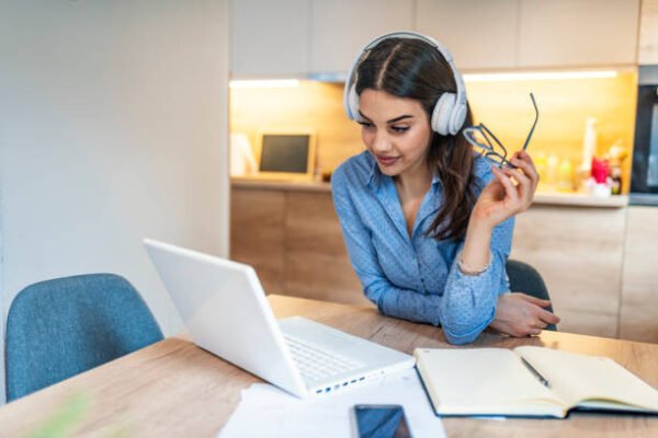 Side view portrait of young businesswoman having business call at home, her workplace, writing down some information. Woman talking on mobile phone, asking questions, looking at pc screen.